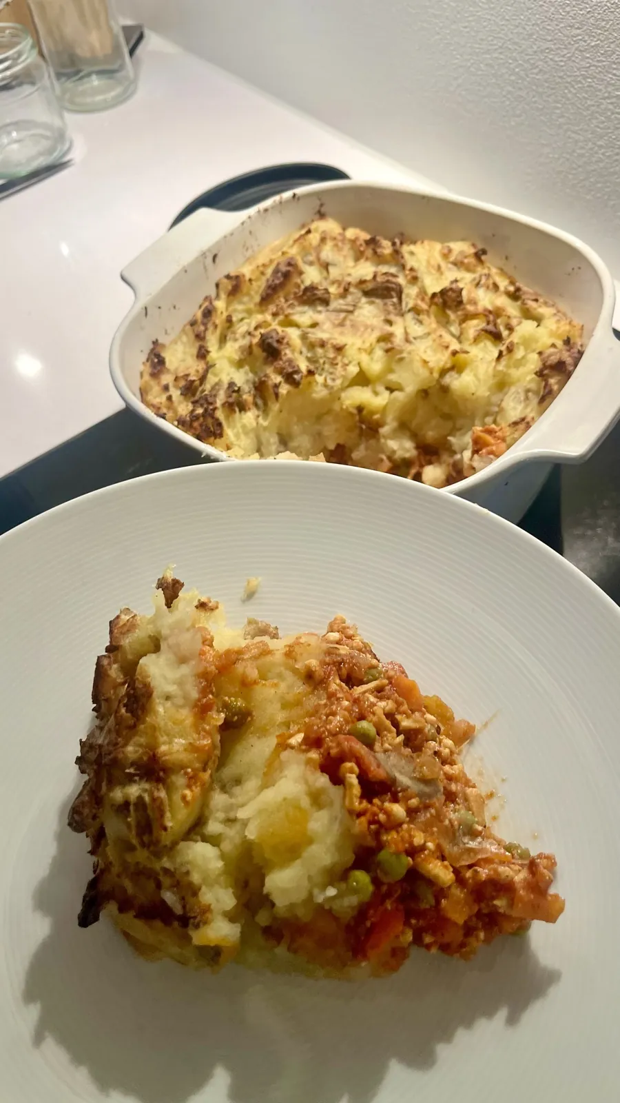 A single serving of BBQ shepherd's pie on a white plate, with the casserole dish in the background